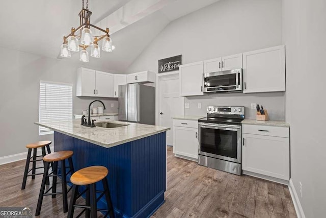 kitchen with stainless steel appliances, a sink, white cabinetry, hanging light fixtures, and an island with sink