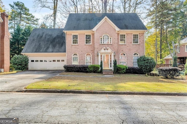 colonial inspired home with a front yard, brick siding, driveway, and an attached garage