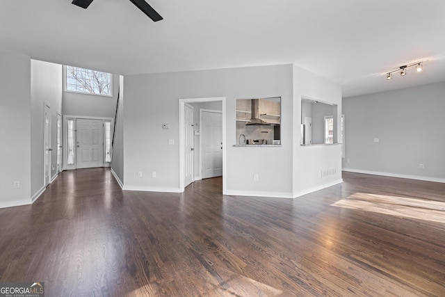 unfurnished living room with a ceiling fan, dark wood-style flooring, a wealth of natural light, and baseboards