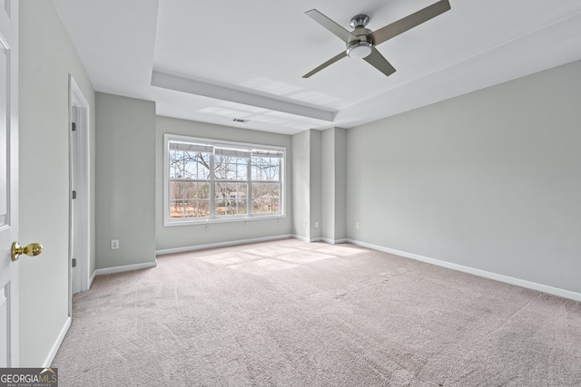 interior space featuring light carpet, visible vents, a ceiling fan, baseboards, and a tray ceiling