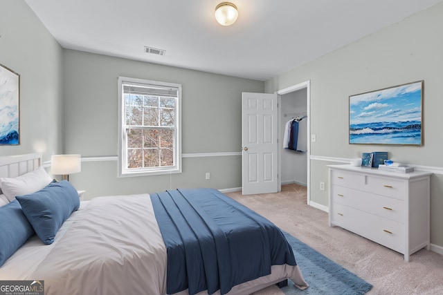 bedroom with light colored carpet, a walk in closet, visible vents, and baseboards