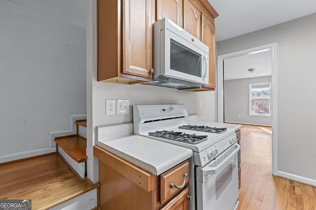 kitchen featuring white appliances, light countertops, baseboards, and light wood finished floors