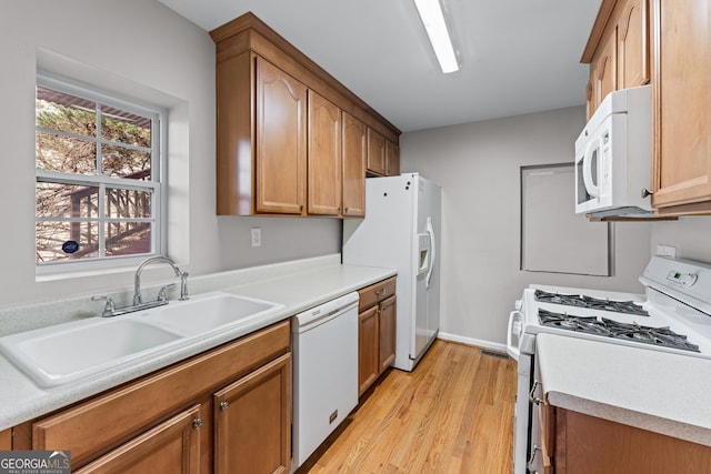 kitchen with light countertops, white appliances, a sink, and brown cabinets