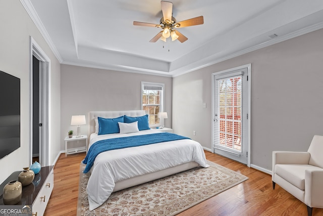 bedroom featuring baseboards, access to outside, a tray ceiling, and wood finished floors