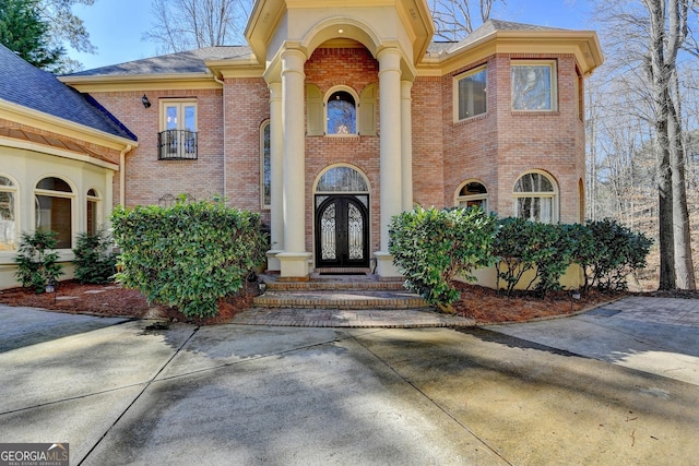 view of exterior entry with french doors, roof with shingles, and brick siding