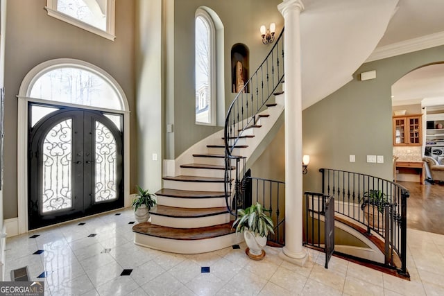 foyer with arched walkways, a towering ceiling, stairs, french doors, and ornamental molding