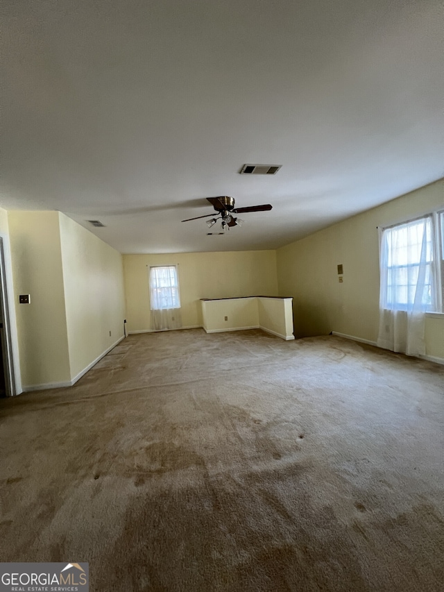 interior space with a wealth of natural light, a ceiling fan, visible vents, and light colored carpet