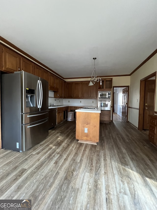 kitchen with pendant lighting, stainless steel appliances, light countertops, ornamental molding, and a kitchen island