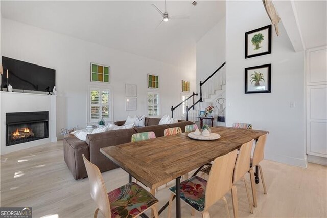 dining space with a warm lit fireplace, a high ceiling, stairs, and light wood-style flooring