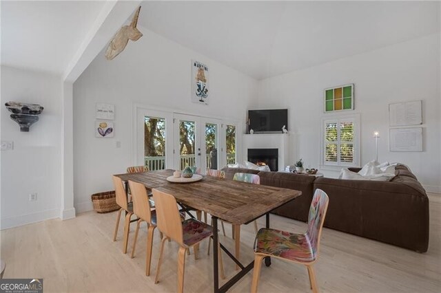 dining area featuring light wood-style floors, a warm lit fireplace, high vaulted ceiling, and baseboards