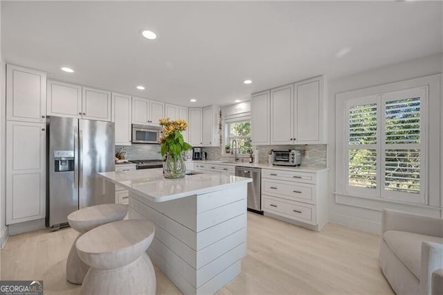 kitchen with light wood finished floors, stainless steel appliances, light countertops, white cabinetry, and backsplash