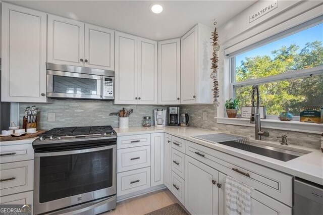 kitchen featuring stainless steel appliances, light countertops, decorative backsplash, white cabinets, and a sink