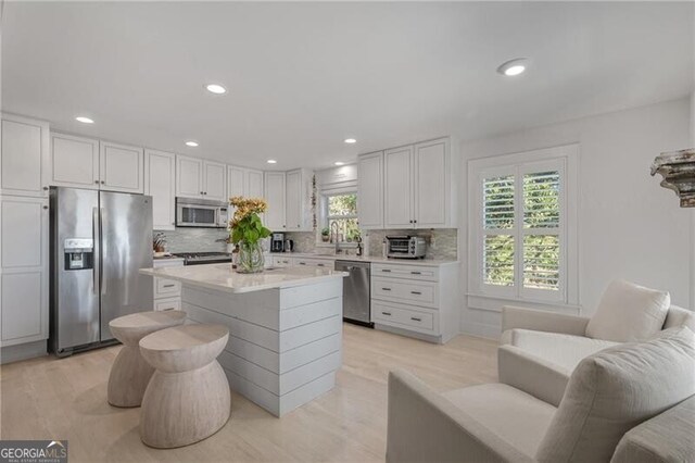 kitchen with tasteful backsplash, light countertops, appliances with stainless steel finishes, white cabinets, and light wood-type flooring