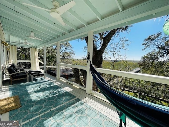 sunroom featuring a healthy amount of sunlight, a ceiling fan, and beamed ceiling