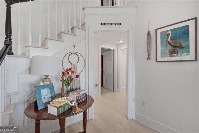 corridor featuring stairway, light wood-type flooring, and baseboards