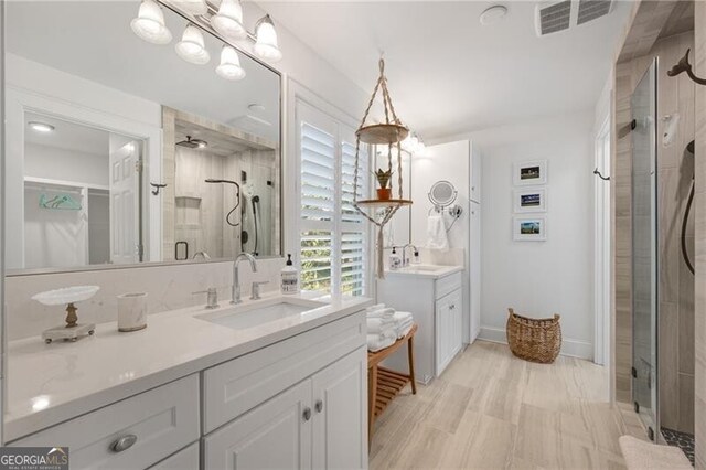 full bath featuring a shower stall, visible vents, two vanities, and a sink