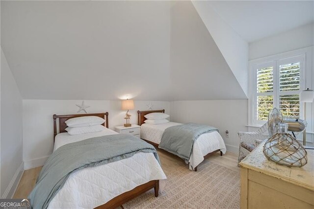 bedroom featuring lofted ceiling, baseboards, and light wood finished floors