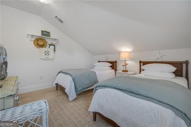 bedroom featuring light wood finished floors, baseboards, visible vents, and vaulted ceiling