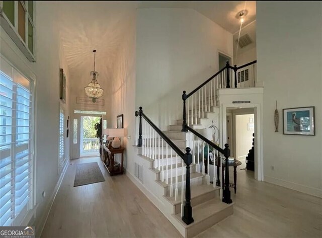 entryway featuring light wood-style flooring, stairway, visible vents, and a towering ceiling