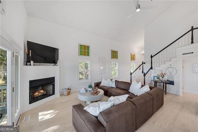 living area with light wood-type flooring, a glass covered fireplace, a high ceiling, and stairs