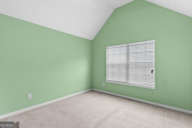 spare room featuring light carpet, vaulted ceiling, and baseboards