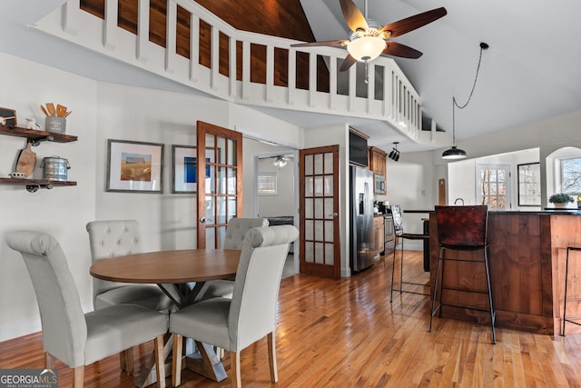 dining space with baseboards, light wood-type flooring, high vaulted ceiling, and ceiling fan