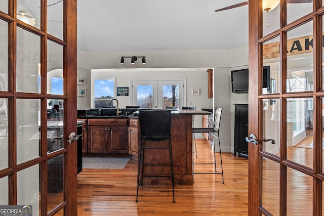 kitchen with french doors, a sink, dark countertops, light wood finished floors, and a peninsula
