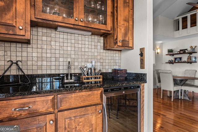 kitchen featuring wine cooler, backsplash, a sink, wood finished floors, and glass insert cabinets