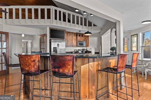 kitchen with a breakfast bar area, lofted ceiling, light wood-type flooring, stainless steel appliances, and brown cabinetry