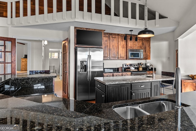 kitchen featuring a sink, appliances with stainless steel finishes, brown cabinets, a kitchen island with sink, and decorative light fixtures