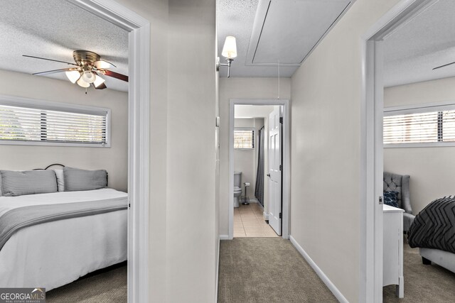 hallway featuring attic access, baseboards, carpet floors, and a textured ceiling