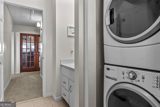 clothes washing area with attic access, stacked washer / drying machine, light tile patterned flooring, light carpet, and laundry area