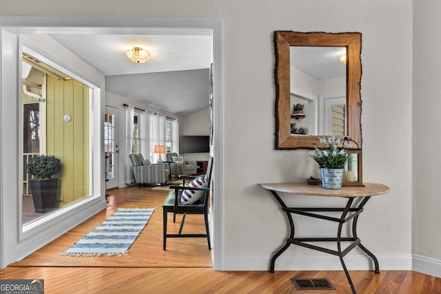 foyer entrance featuring visible vents, baseboards, lofted ceiling, and wood finished floors