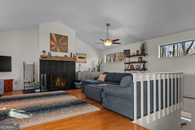 living room featuring a ceiling fan, vaulted ceiling, a fireplace, and wood finished floors
