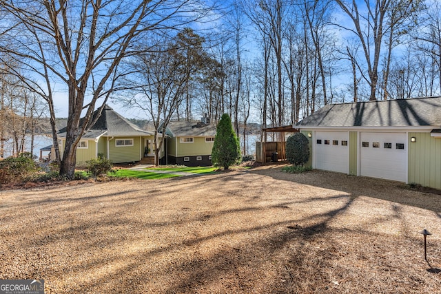 exterior space featuring dirt driveway, a shingled roof, and a garage