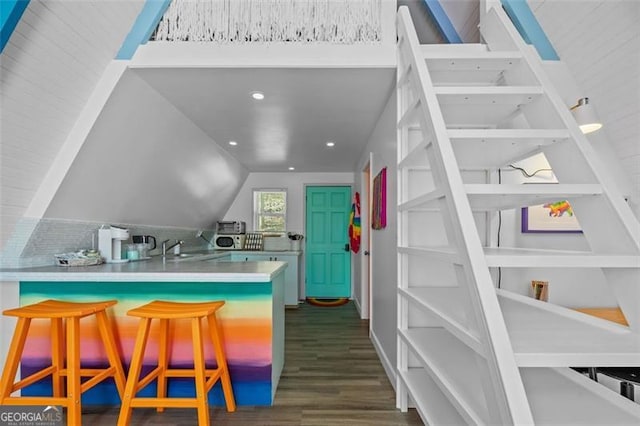 kitchen with lofted ceiling, a peninsula, light countertops, a kitchen bar, and dark wood finished floors