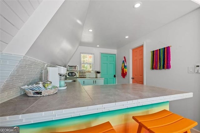 kitchen featuring tile countertops, lofted ceiling, a toaster, recessed lighting, and a peninsula