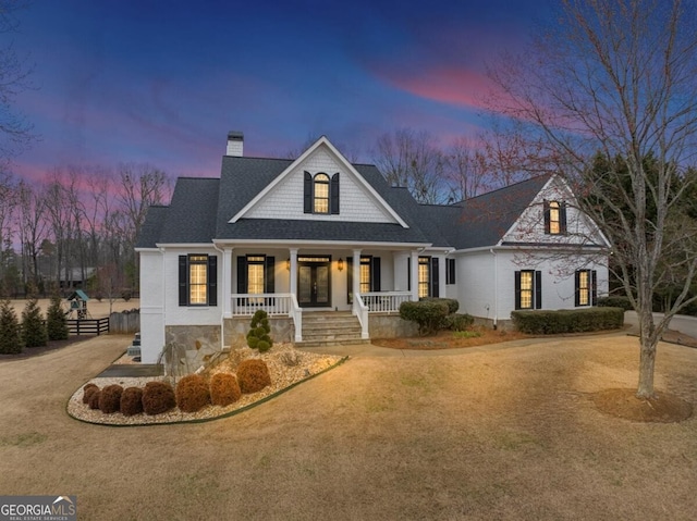 view of front facade featuring covered porch, a shingled roof, a chimney, and a front yard