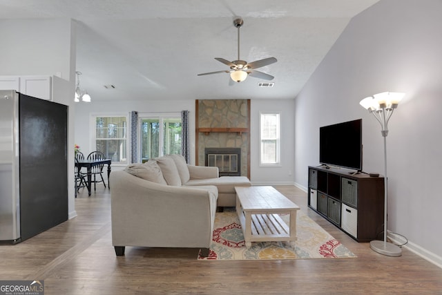 living room with a wealth of natural light, vaulted ceiling, a stone fireplace, and wood finished floors