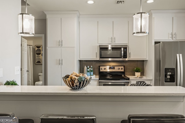 kitchen featuring tasteful backsplash, white cabinetry, stainless steel appliances, and decorative light fixtures