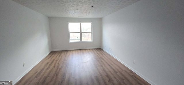 spare room featuring a textured ceiling, wood finished floors, and baseboards