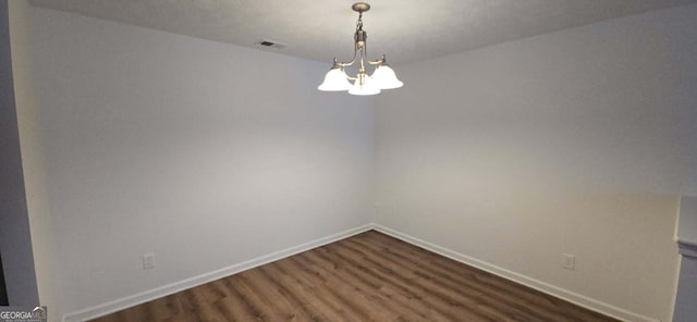 spare room featuring dark wood-style flooring, an inviting chandelier, visible vents, and baseboards