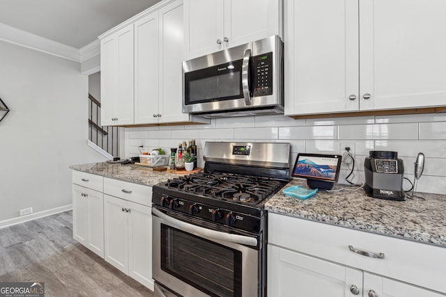 kitchen with white cabinets, decorative backsplash, appliances with stainless steel finishes, ornamental molding, and light stone countertops