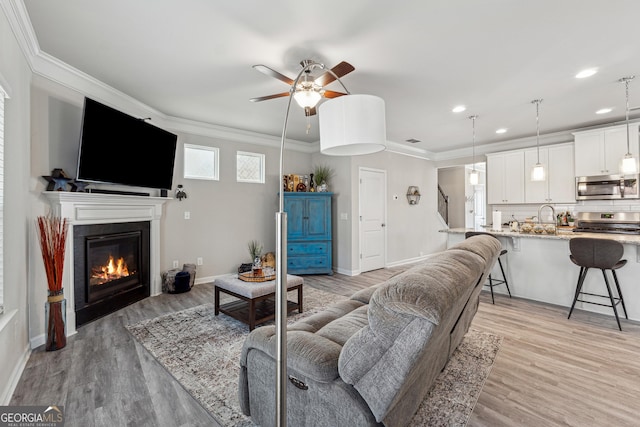 living area featuring ornamental molding, a glass covered fireplace, baseboards, and light wood finished floors