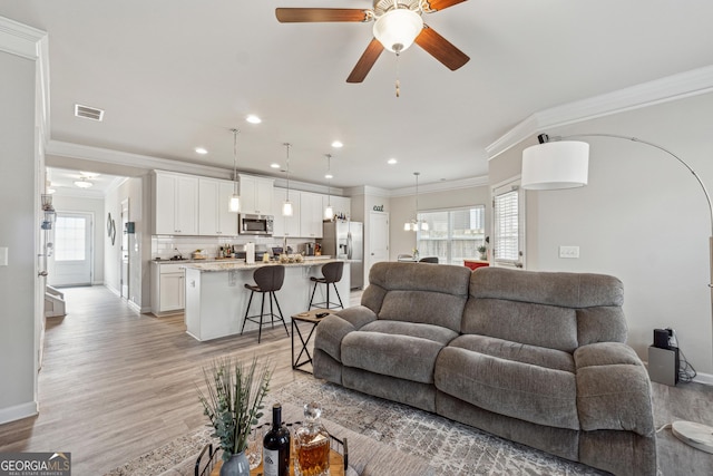 living area featuring light wood-style floors, crown molding, visible vents, and a wealth of natural light