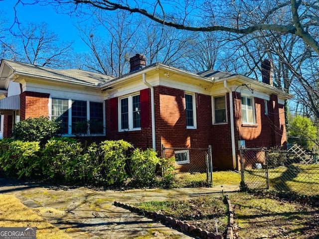 view of side of home featuring a fenced front yard, brick siding, and a chimney