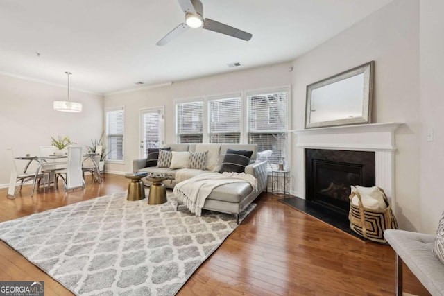 living area featuring a ceiling fan, a glass covered fireplace, baseboards, and wood finished floors