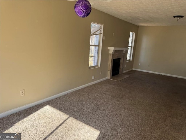 unfurnished living room with a tiled fireplace, baseboards, dark colored carpet, and a textured ceiling