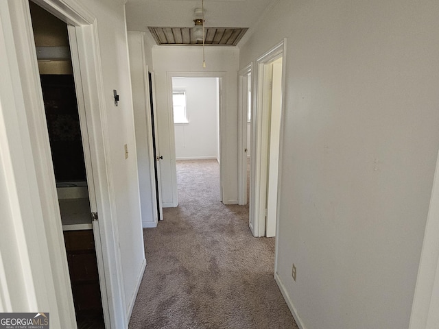 corridor with baseboards, attic access, and light colored carpet