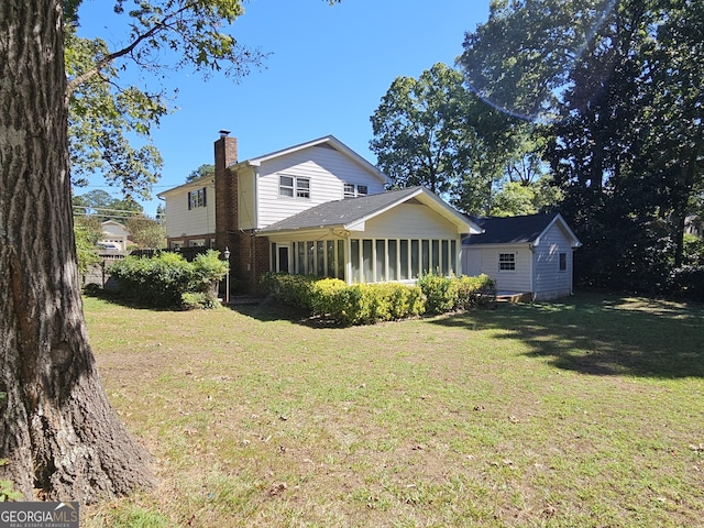 back of property featuring a sunroom, brick siding, a lawn, and a chimney